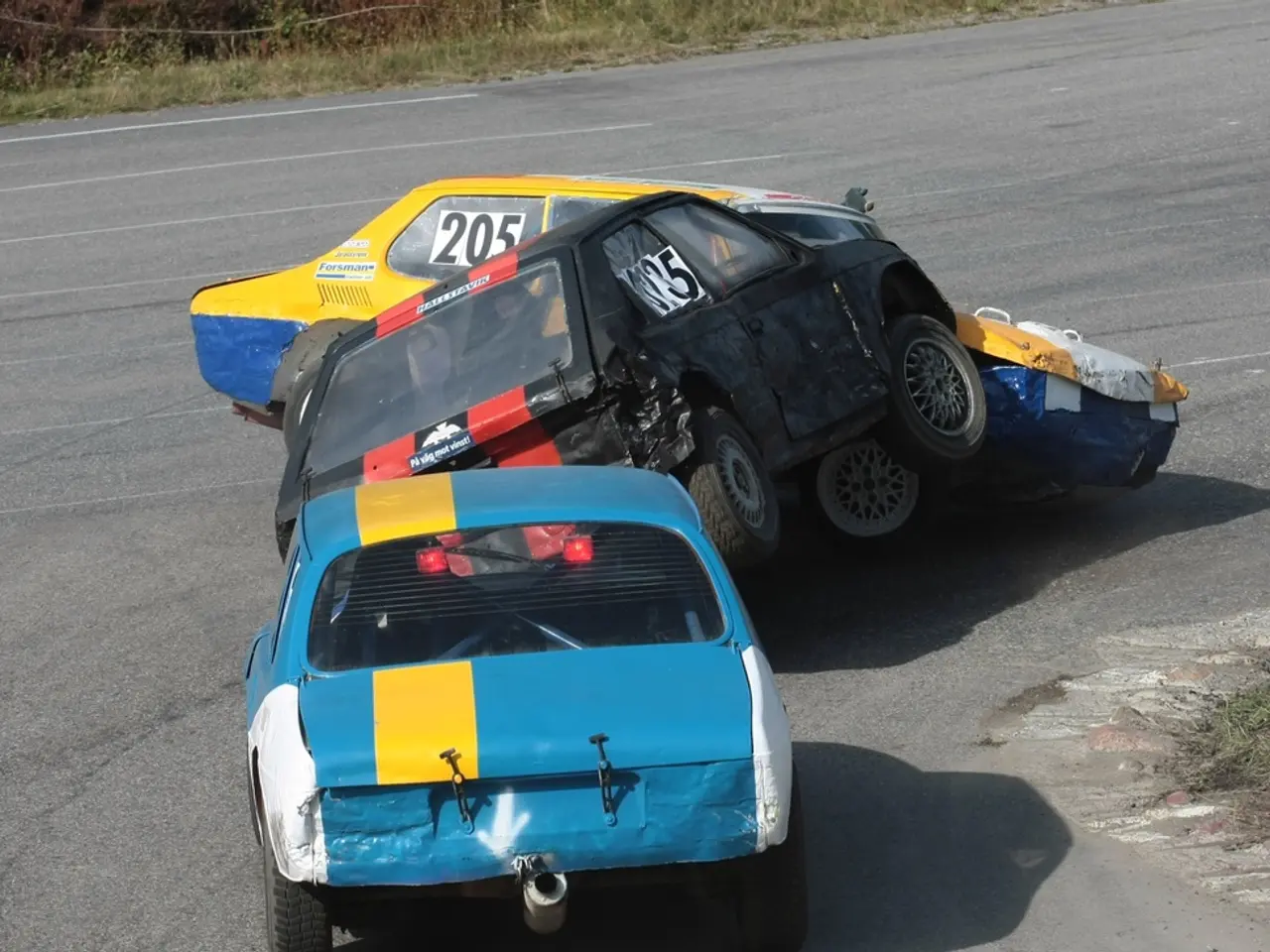 In this image there are three cars on the road which are crashing one another. In the background...