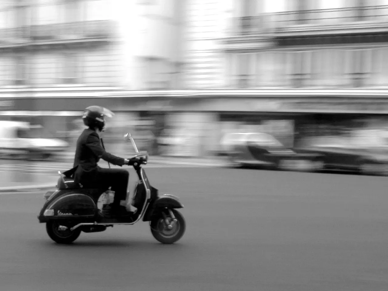 In this image i can see a person riding scooter on the road.