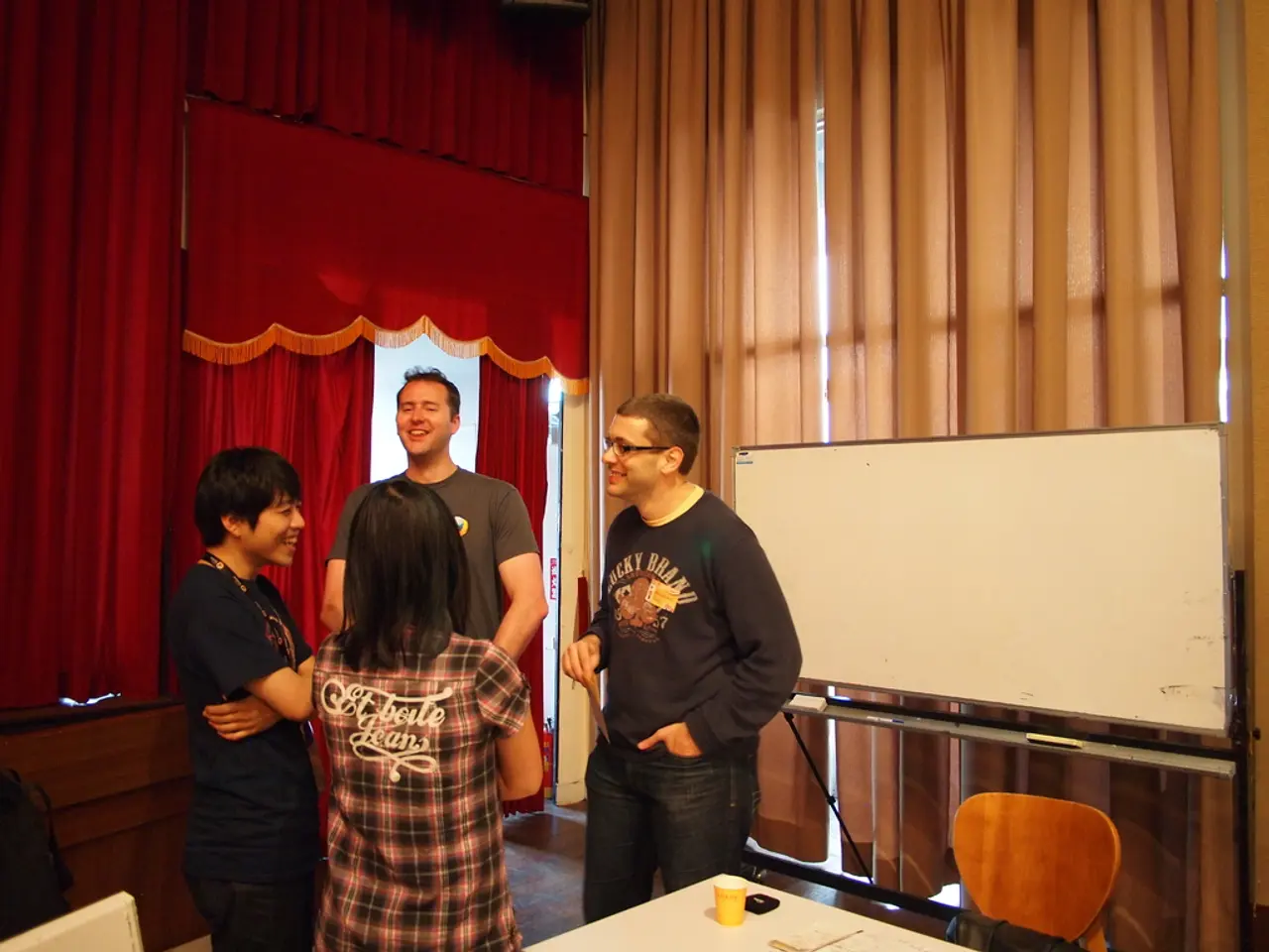 there are 4 people standing, talking to each other. behind them there are red and brown curtains