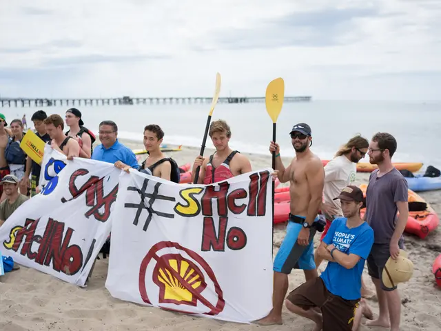 In this image there are group of people standing in the sand by holding the banners. In the...
