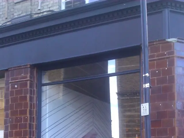 In this image we can see one building with glass windows, one white wall decorated, one light with...