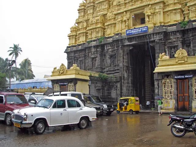 In this picture we can see temple, in front few vehicles are placed, few people are walking, around...