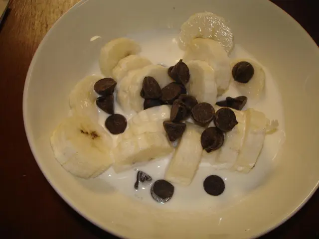 In this image I can see a bowl in which sliced bananas, chocolate chips and milk is there which is...